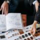 Deux personnes consultent un catalogue de modèles et des nuanciers de matières pour personnaliser une production textile