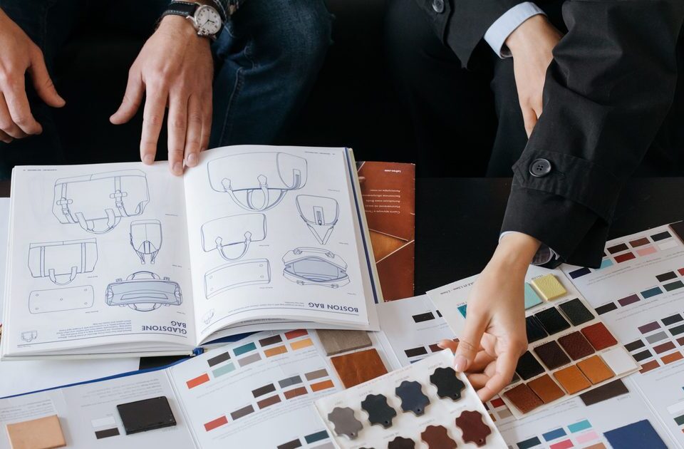 Deux personnes consultent un catalogue de modèles et des nuanciers de matières pour personnaliser une production textile
