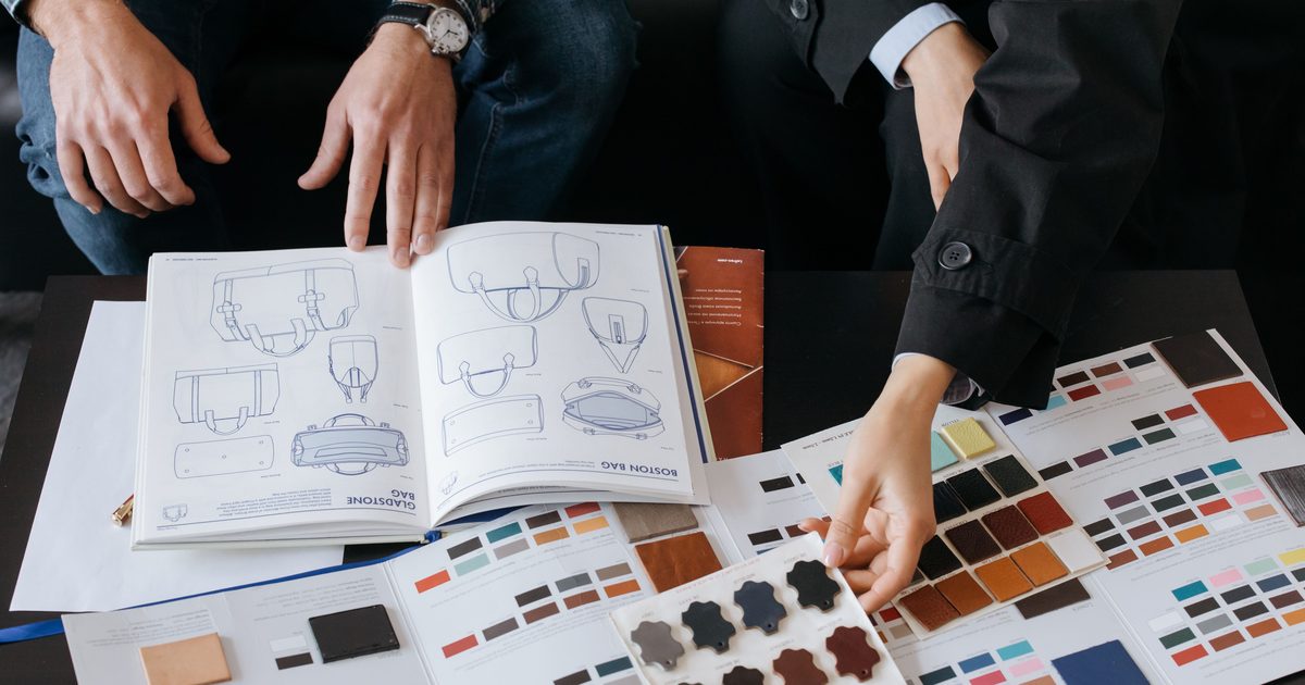 Deux personnes consultent un catalogue de modèles et des nuanciers de matières pour personnaliser une production textile