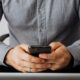 Gros plan sur des mains tenant un smartphone pour vérifier le tarif d'un appel vers un numéro 0825