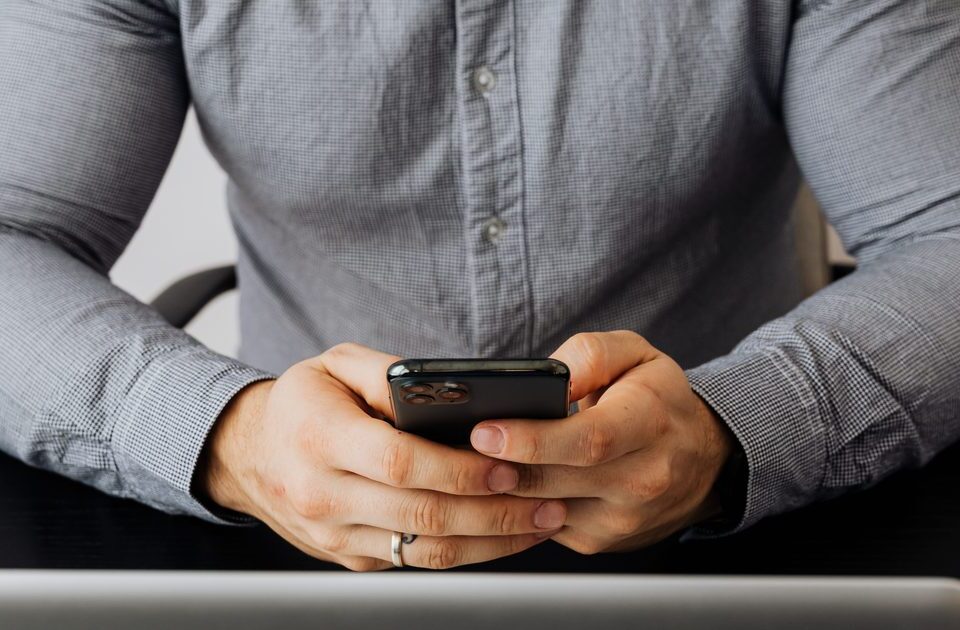 Gros plan sur des mains tenant un smartphone pour vérifier le tarif d'un appel vers un numéro 0825