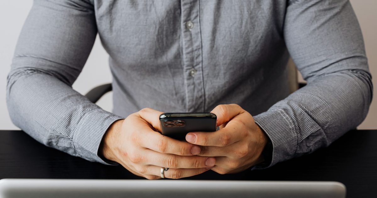 Gros plan sur des mains tenant un smartphone pour vérifier le tarif d'un appel vers un numéro 0825