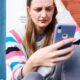 Femme assise devant chez elle regardant son smartphone avec inquiétude après un appel suspect en 0891