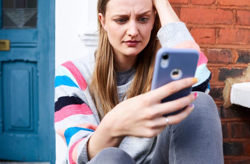 Femme assise devant chez elle regardant son smartphone avec inquiétude après un appel suspect en 0891