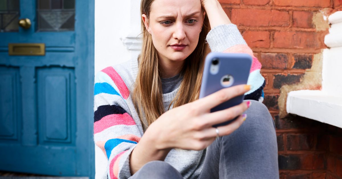 Femme assise devant chez elle regardant son smartphone avec inquiétude après un appel suspect en 0891